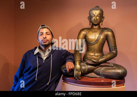 Nepal, Patan Museum.  Nepali hält sein Handy stehen neben einem Buddha in der Haltung des Sieges. Stockfoto