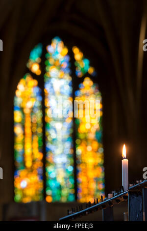 Einzigen beleuchteten Gebet Kerze vor einem modernen Glasfenster in der Abtei von Tewkesbury, Gloucestershire, England Stockfoto