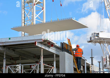 Website der Bauarbeiter auf Leiter als Kran Positionen großen Betonfertigteile Betonboden Panel auf neues Appartementhaus Gebäude in South London England UK Stockfoto