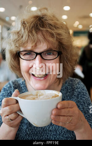 Bei einer Tasse Cappuccino Kaffee in einem Café die Sahne auf ihren Lippen und Nase Woman applying Stockfoto