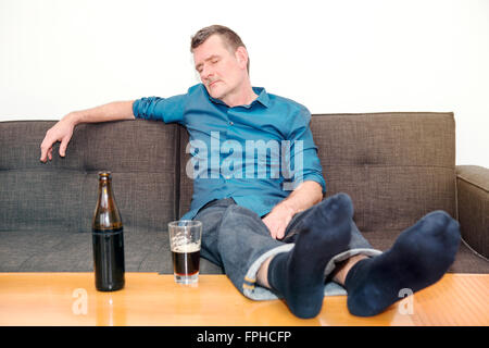 ältere Menschen schlafen auf der Couch mit einer Flasche Bier auf dem Tisch Stockfoto