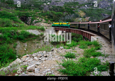 White Pass Railroad Elektromotor zieht Zug Pkw über Trestle Bridge in Richtung Tunnel in den Felsen. Stockfoto