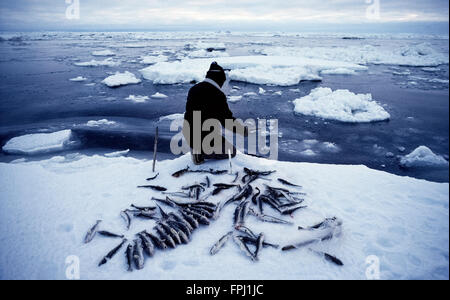 Eine Native Alaskan fischt mit einer einfachen sind am Rande einer Eisscholle in der Beringsee während eines bewölkten Midwinter in Nome, Alaska, USA. Stockfoto