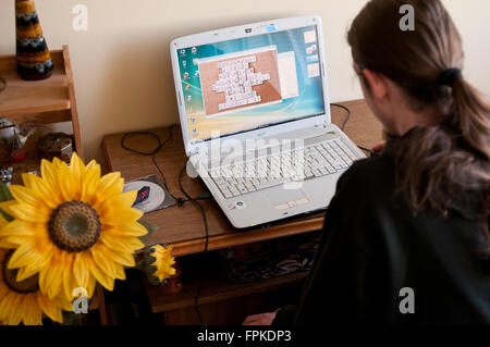 Mann Spiel Mahjong-Titans auf dem Laptop, schwarz gekleidet lange Haare jungen Menschen im Raum während Urlaub Freizeit Stockfoto
