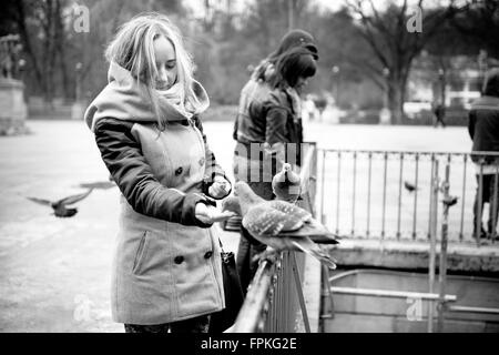 Frau füttern Tauben im Park in Polen, hungrige Vögel auf dem Zaun, Essen aus der Hand und andere Menschen hinter, Winterzeit Stockfoto