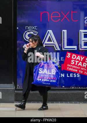 Frau, die Modewaren in einer Einkaufstasche trägt, gekauft beim nächsten Bekleidungsgeschäft Half Price Sale Event in Chester, Großbritannien Stockfoto