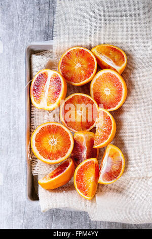 Sizilianischen Blut Orangen Früchte in Aluminium Tablett mit weißen Sackleinen über grauen Hintergrund aus Holz geschnitten. Ansicht von oben Stockfoto