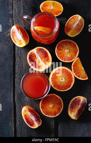 In Scheiben geschnitten sizilianischen Blutorangen in Türkis Keramik Teller und Glas frischen roten Orangensaft über alten Holztisch. Dunkel rustikal Stockfoto