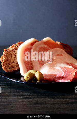 Italienischer Schinken. Dünne Stücke Schweinefleisch in der Nähe von Brot und Oliven Stockfoto