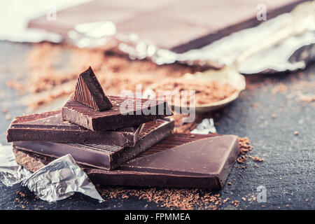 Schokolade. Schwarze Schokolade. Ein paar Würfel von schwarzer Schokolade. Schokolade Tafeln von geriebener Schokolade Pulver verschüttet. Kaffeebohnen. Stockfoto