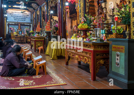 Hanoi, Vietnam. Frauen, die im Inneren der alten Tran Quoc buddhistische Pagode vor einer verzierten Schrein beten Stockfoto