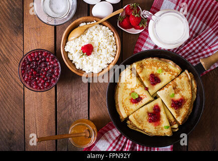 Goldene Pfannkuchen mit Preiselbeermarmelade und Honig im rustikalen Stil. Ansicht von oben Stockfoto