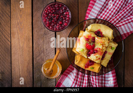 Goldene Pfannkuchen mit Preiselbeermarmelade und Honig im rustikalen Stil. Ansicht von oben Stockfoto