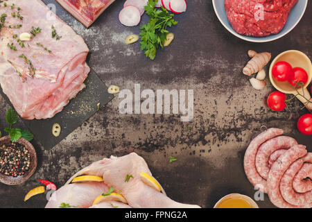 Rohes Fleisch-Sortiment. Verschiedene Arten von Fleisch mit Gemüse und Gewürzen auf dunklem Hintergrund Stockfoto