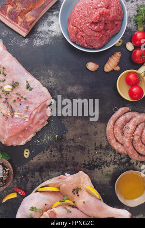 Rohes Fleisch-Sortiment. Verschiedene Arten von Fleisch mit Gemüse und Gewürzen auf dunklem Hintergrund Stockfoto