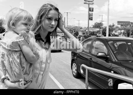 eine junge Mutter mit Baby wartet überqueren eine viel befahrenen Straße in Brisbane, Queensland, Australien Stockfoto