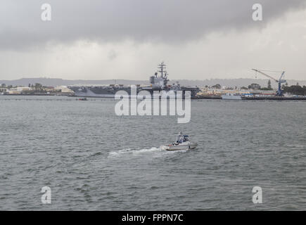 Ein Shelter Island Polizei-Boot ist auf Patrouille im Hafen von San Diego mit dem Flugzeugträger USS Ronald Reagan im Hintergrund. Stockfoto