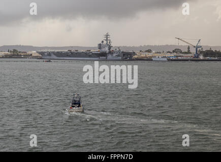 Ein Shelter Island Polizei-Boot ist auf Patrouille im Hafen von San Diego mit dem Flugzeugträger USS Ronald Reagan im Hintergrund. Stockfoto