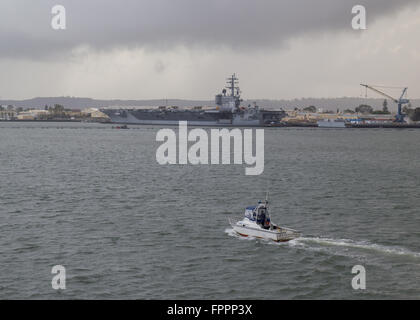 Ein Shelter Island Polizei-Boot ist auf Patrouille im Hafen von San Diego mit dem Flugzeugträger USS Ronald Reagan im Hintergrund. Stockfoto