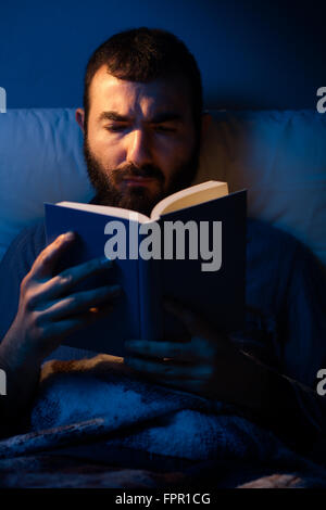 Mann liest ein Buch in der Nacht in einem Bett Stockfoto