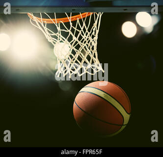 Basketball wird durch den Reifen bei einer Sportarena (vorsätzliche Spotlight) Stockfoto