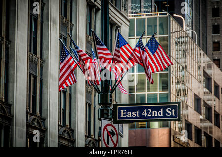 East 42nd St Zeichen und Gruppe von amerikanischen Flaggen auf Laternenpfahl, New York City, USA. Stockfoto