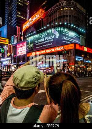 Paar, die ein Foto auf einem ipad von Times Square in der Nacht, New York City, USA. Stockfoto