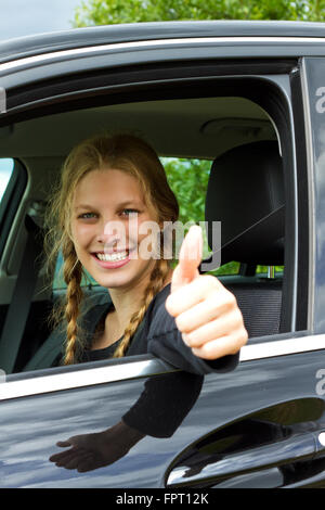 Glücklich, junge Frau in einem Auto in der Straße und Gestikulieren Daumen treiben Stockfoto