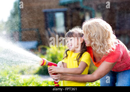 Kleine Gärtner-Mädchen mit Mutter Bewässerung auf Rasen in der Nähe von Haus Stockfoto