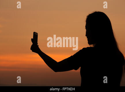 Silhouette der Frau im Sonnenuntergang nehmen Foto mit Handy Stockfoto