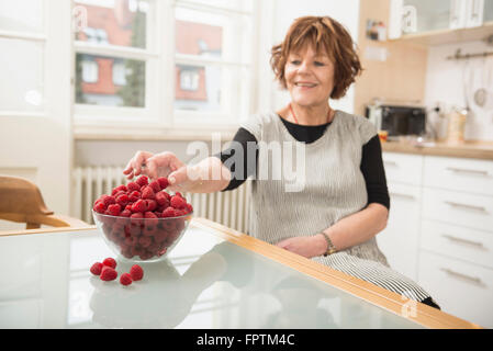 Ältere Frau Nibbeln Himbeeren in der Küche, München, Bayern, Deutschland Stockfoto