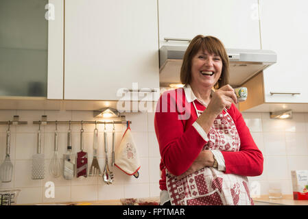 Beautiful senior Woman trägt Schürze und trinken Espresso-Kaffeemaschine in der Küche, München, Bayern, Deutschland Stockfoto