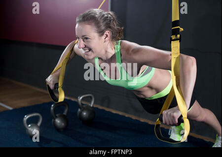 Sportliche junge Frau macht Liegestütze in der Turnhalle mit TRX Gürtel, Bayern, Deutschland Stockfoto