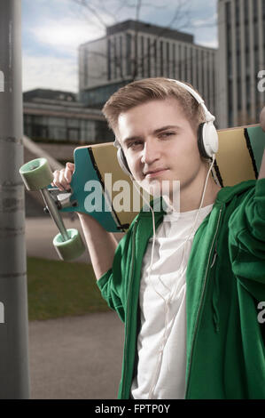 Junge mit Skateboard auf Schultern und hören Musik auf der Straße, Bayern, Deutschland Stockfoto