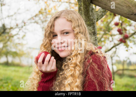 Porträt eines blonden Mädchens Essen eines Apfels in einem Apple Orchard Bauernhof, Bayern, Deutschland Stockfoto