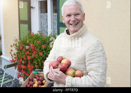 Reifer Mann Äpfel in den Händen vor Vollwert-Shop hält und lächelnd, Bayern, Deutschland Stockfoto