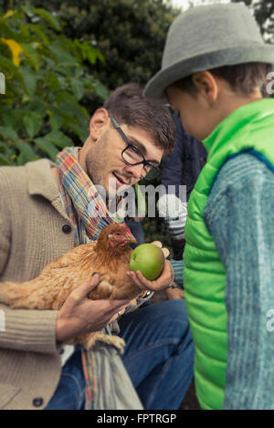 Vater hält ein Huhn Vogel und Sohn Fütterung Apple, Bayern, Deutschland, Stockfoto