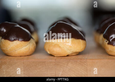 Windbeutel mit Ganache in Reihen auf einen hölzernen Butcher Block Oberfläche Stockfoto