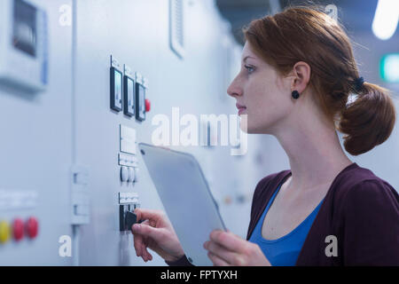 Junge weibliche engineer Update Systemsteuerung durch digital-Tablette in einer Branche, Freiburg Im Breisgau, Baden-Württemberg, Deutschland Stockfoto