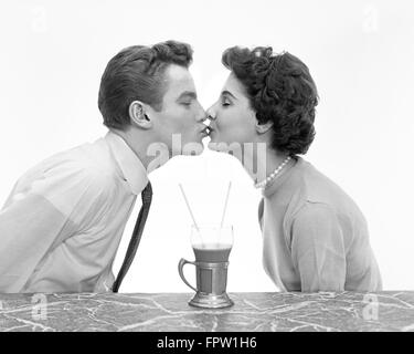 1950ER JAHREN PAAR MANN FRAU KÜSSEN ROMANISCHEN PROFILDATUM IN MARMOR ZÄHLER EIN GETRÄNK MALT SHAKE MIT ZWEI STROHHALMEN ANTEIL TEENS TEENAGER Stockfoto