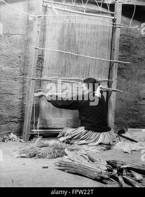 1930ER JAHREN INDIANISCHE NAVAJO FRAU SITZT AM WEBSTUHL WEBEN EINES TEPPICHS Stockfoto