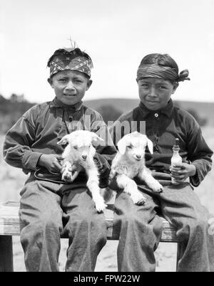 1930ER JAHREN ZWEI INDIANISCHE NAVAJO JUNGEN BLICK AUF KAMERA HOLDING ZWEI BABY LÄMMER NEW MEXICO USA Stockfoto