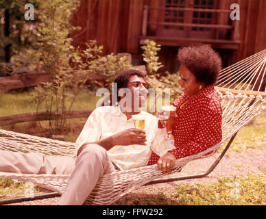 1970ER JAHREN AFRIKANISCHE AMERIKANISCHE PAAR MANN FRAU IN HÄNGEMATTE TRINKEN BIER AUßERHALB LIEGENDE Stockfoto