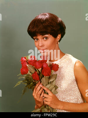 1970ER JAHREN AFROAMERIKANISCHE FRAU MIT PAILLETTEN BLUSE STRAUß ROTER ROSEN, BLICK IN DIE KAMERA HALTEN Stockfoto
