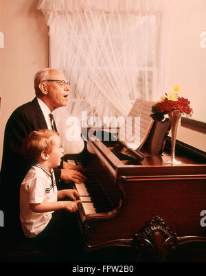 1970ER JAHRE ALTEN GROßVATER UND JUNGEN ENKEL SINGEN UND SPIELEN EINEN FLÜGEL Stockfoto