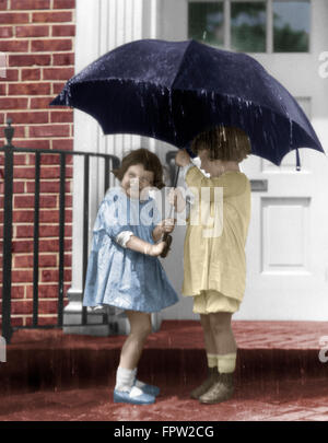 1920ER JAHREN PAAR KLEINE MÄDCHEN STEHEN AUF VORDERSEITE BÜCKEN UNTER DACH IM STRÖMENDEN REGEN Stockfoto