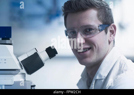 Porträt eines jungen männlichen Wissenschaftlers Mikroskop in einem optischen Labor, Freiburg Im Breisgau, Baden-Württemberg, Deutschland Stockfoto