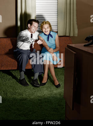 1950ER JAHREN PAAR IM ABGEDUNKELTEN WOHNZIMMER FERNSEHEN MIT MANN ZEIGTE AUF BILDSCHIRM Stockfoto