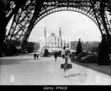 1920ER JAHREN FRAU ZU FUß UNTER DEM EIFFELTURM MIT DEM TROCADERO IN HINTERGRUND PARIS FRANKREICH Stockfoto