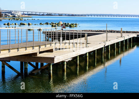 Ein hölzerner Pier erstreckt sich in das Meer mit der Öland-Brücke im Hintergrund. Stockfoto